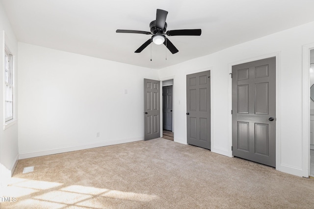 unfurnished bedroom featuring ceiling fan, light colored carpet, and multiple closets