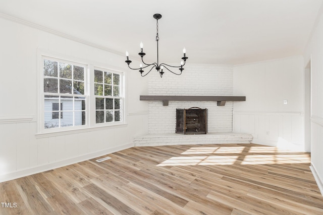 unfurnished living room featuring hardwood / wood-style floors, an inviting chandelier, a brick fireplace, and crown molding