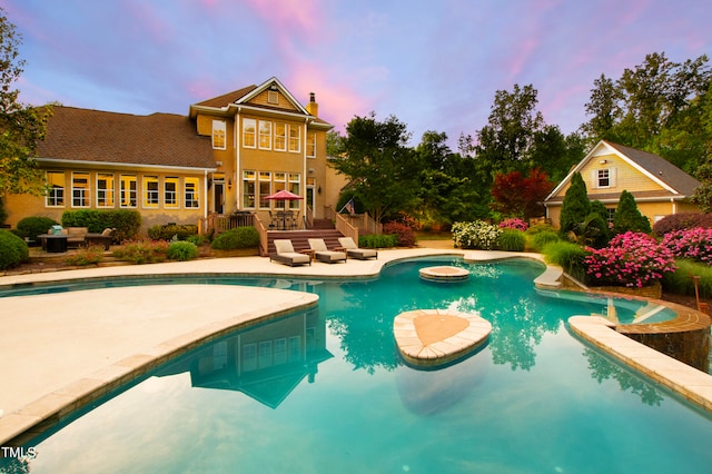 pool at dusk featuring a hot tub and a patio