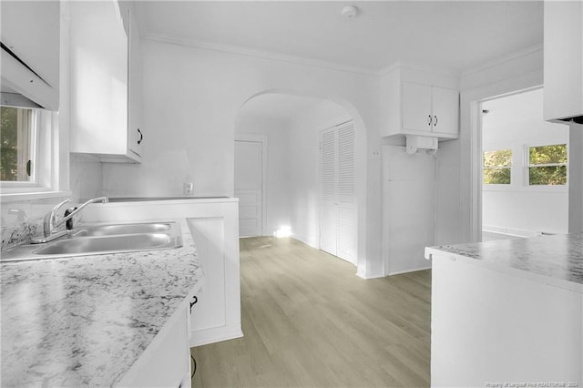 kitchen with sink, white cabinetry, light stone counters, ornamental molding, and light hardwood / wood-style flooring