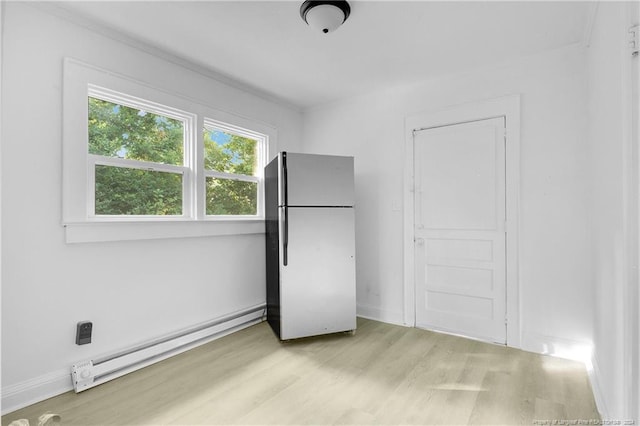 unfurnished bedroom featuring a baseboard heating unit, light hardwood / wood-style flooring, fridge, and a closet