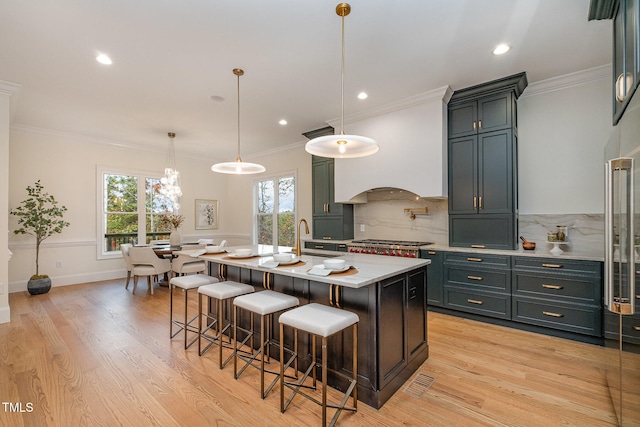 kitchen featuring light wood-type flooring, a kitchen bar, backsplash, pendant lighting, and a center island with sink