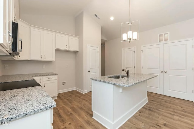 kitchen with white cabinetry, sink, pendant lighting, lofted ceiling, and a center island with sink