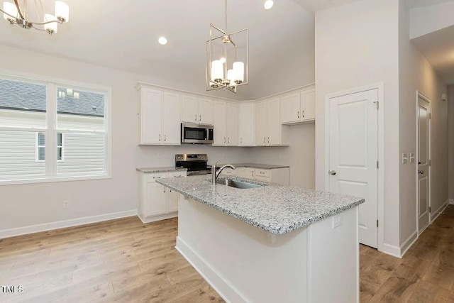 kitchen featuring white cabinetry, light stone countertops, an island with sink, appliances with stainless steel finishes, and light wood-type flooring