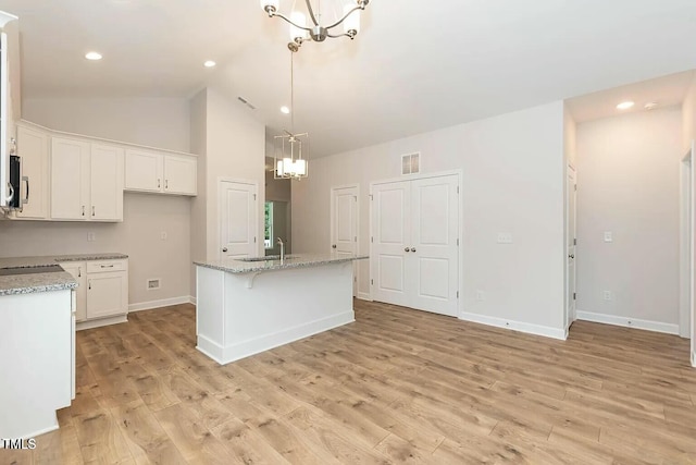 kitchen with white cabinetry, an inviting chandelier, light stone counters, an island with sink, and light wood-type flooring