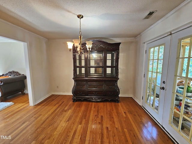 unfurnished dining area featuring french doors, ornamental molding, a textured ceiling, a notable chandelier, and hardwood / wood-style flooring