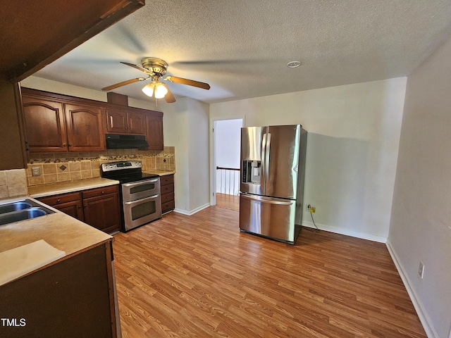 kitchen featuring stainless steel appliances, backsplash, a textured ceiling, exhaust hood, and light hardwood / wood-style flooring