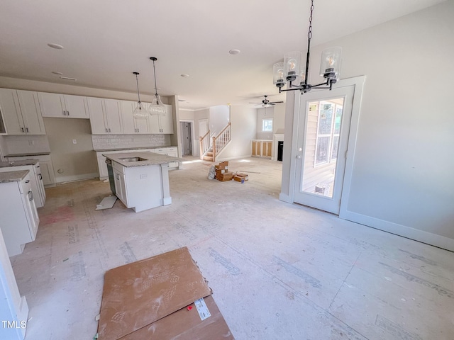 kitchen with light stone counters, white cabinets, decorative light fixtures, decorative backsplash, and a kitchen island