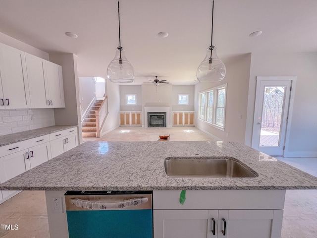 kitchen featuring a center island with sink, white cabinetry, stainless steel dishwasher, and decorative light fixtures