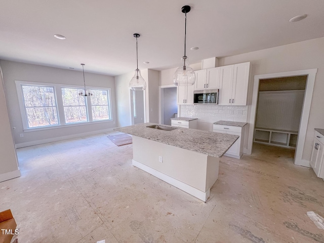 kitchen with a center island with sink, light stone counters, white cabinetry, hanging light fixtures, and decorative backsplash