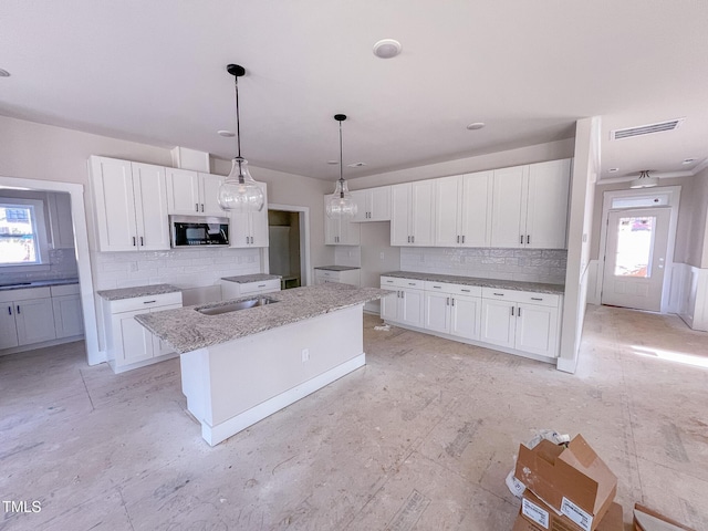 kitchen featuring light stone countertops, decorative light fixtures, a center island, backsplash, and white cabinetry