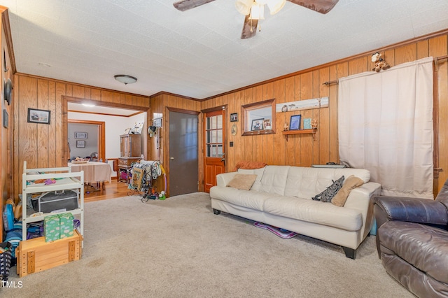 carpeted living room featuring ceiling fan, ornamental molding, and wood walls