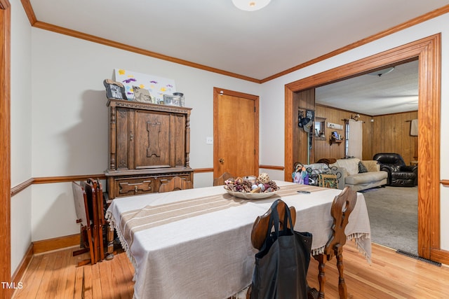 dining area with light wood-type flooring, crown molding, and wooden walls