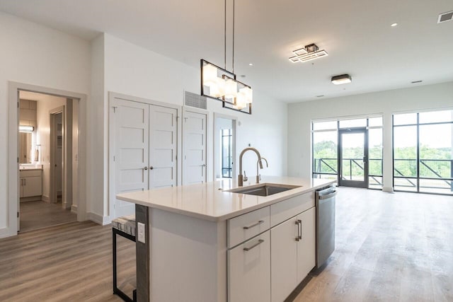 kitchen with white cabinetry, light hardwood / wood-style flooring, stainless steel dishwasher, an island with sink, and decorative light fixtures