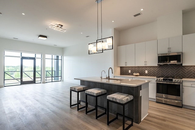 kitchen with decorative light fixtures, light hardwood / wood-style floors, an island with sink, and appliances with stainless steel finishes