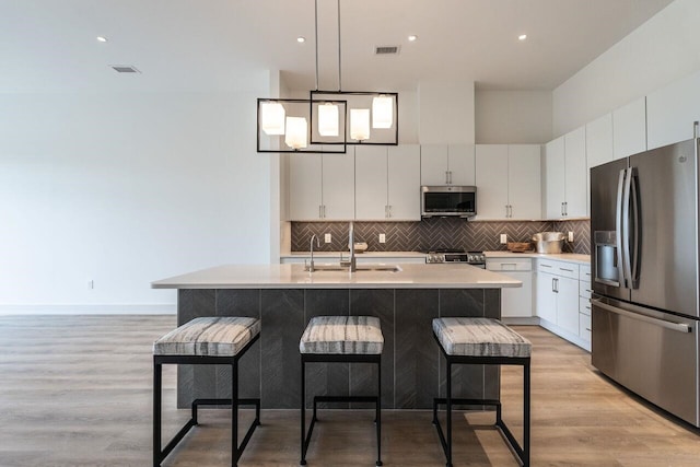 kitchen with a center island with sink, white cabinetry, stainless steel appliances, and light hardwood / wood-style flooring