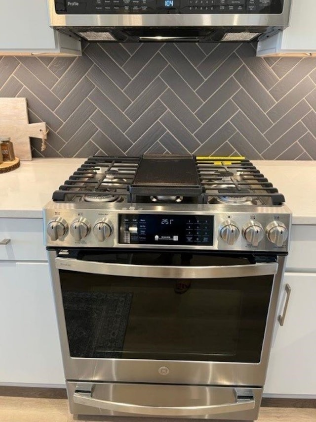 interior details with white cabinets, decorative backsplash, and high end stainless steel range