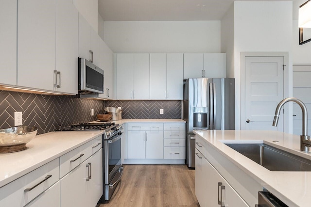 kitchen featuring stainless steel appliances, white cabinetry, light hardwood / wood-style floors, and sink