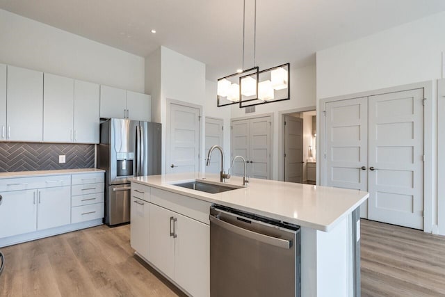 kitchen featuring a center island with sink, white cabinets, sink, hanging light fixtures, and stainless steel appliances