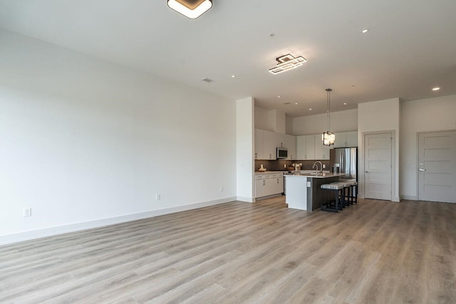 kitchen with pendant lighting, light wood-type flooring, a breakfast bar, a center island with sink, and appliances with stainless steel finishes