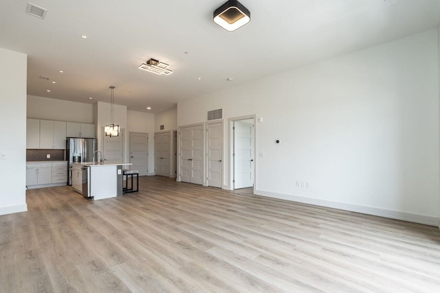 kitchen with a center island with sink, decorative light fixtures, light hardwood / wood-style floors, and tasteful backsplash