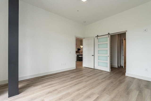 unfurnished bedroom with a barn door and light hardwood / wood-style floors