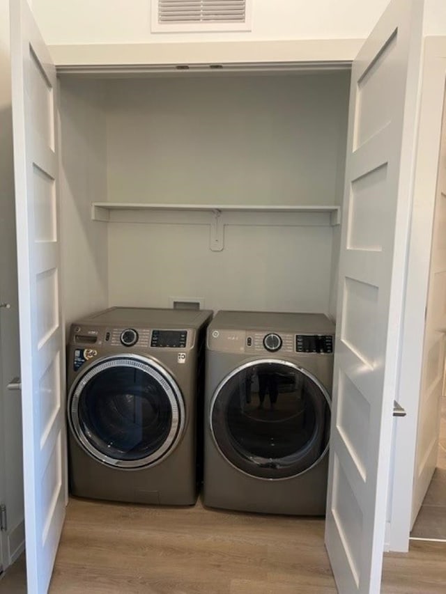 clothes washing area with light hardwood / wood-style flooring and washer and clothes dryer