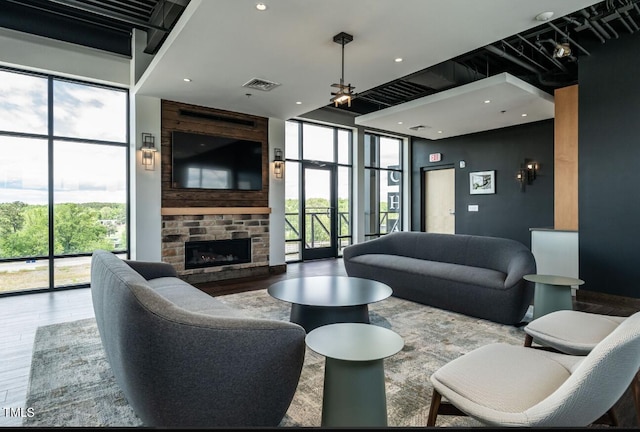 living room with wood-type flooring, a stone fireplace, plenty of natural light, and ceiling fan