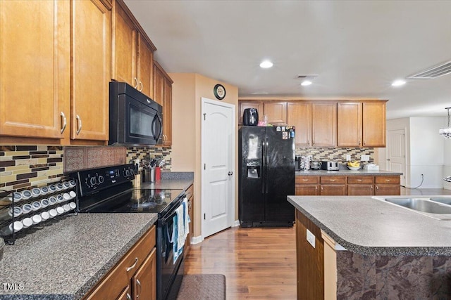 kitchen with decorative backsplash, hardwood / wood-style flooring, black appliances, and sink