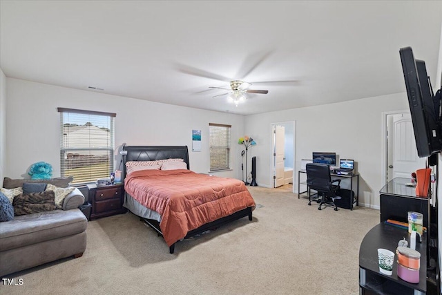 bedroom with ensuite bathroom, light colored carpet, and ceiling fan