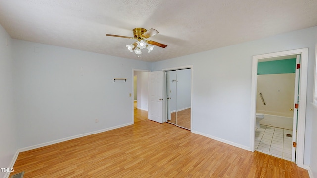 unfurnished bedroom with light hardwood / wood-style floors, a textured ceiling, connected bathroom, ceiling fan, and a closet