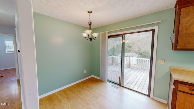 unfurnished dining area with an inviting chandelier, plenty of natural light, light hardwood / wood-style flooring, and a textured ceiling