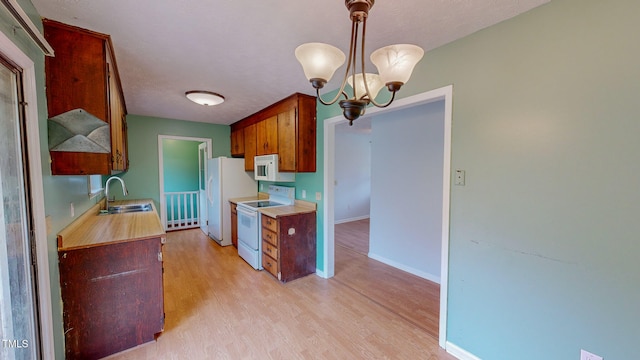 kitchen with hanging light fixtures, a chandelier, sink, light wood-type flooring, and white appliances