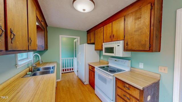 kitchen featuring white appliances, a textured ceiling, sink, and light hardwood / wood-style floors