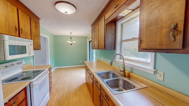 kitchen with a notable chandelier, hanging light fixtures, sink, light hardwood / wood-style floors, and white appliances