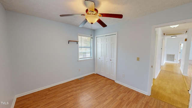 unfurnished bedroom featuring ceiling fan, a textured ceiling, a closet, and light hardwood / wood-style flooring