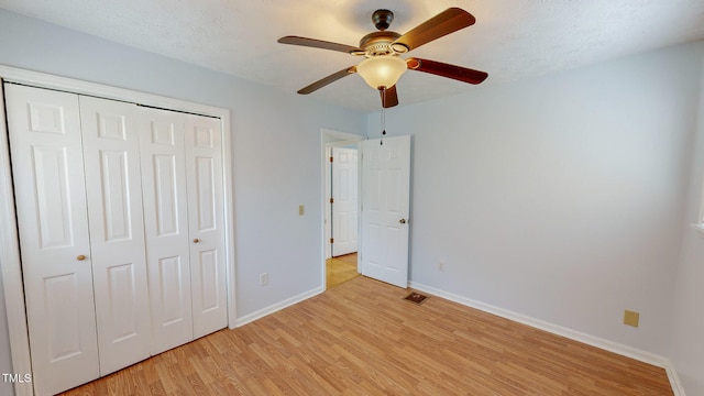 unfurnished bedroom featuring a closet, light wood-type flooring, a textured ceiling, and ceiling fan