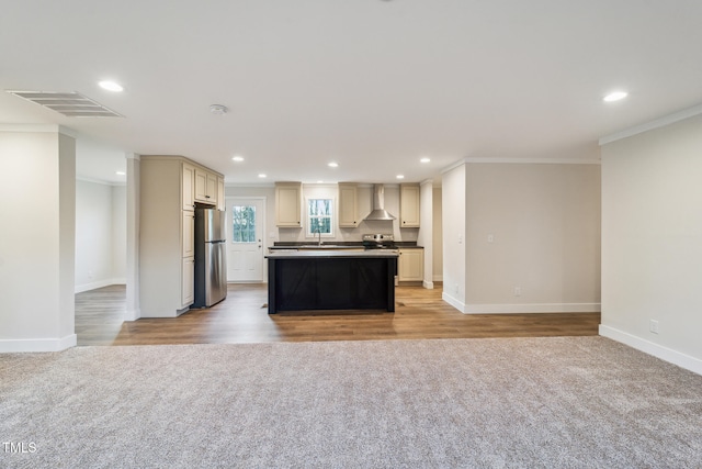 kitchen with sink, appliances with stainless steel finishes, ornamental molding, a kitchen island, and wall chimney range hood