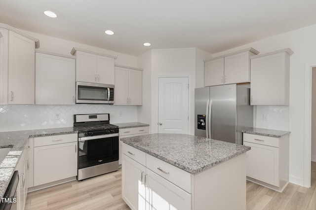 kitchen with white cabinets, light hardwood / wood-style floors, a kitchen island, and appliances with stainless steel finishes