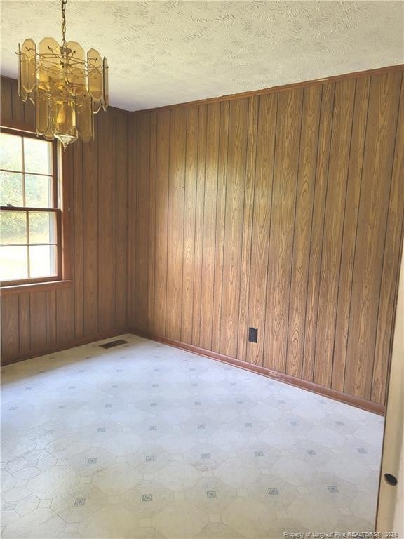 empty room with wooden walls, a textured ceiling, and an inviting chandelier