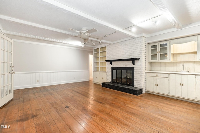 unfurnished living room with a fireplace, ceiling fan, light hardwood / wood-style floors, track lighting, and built in shelves