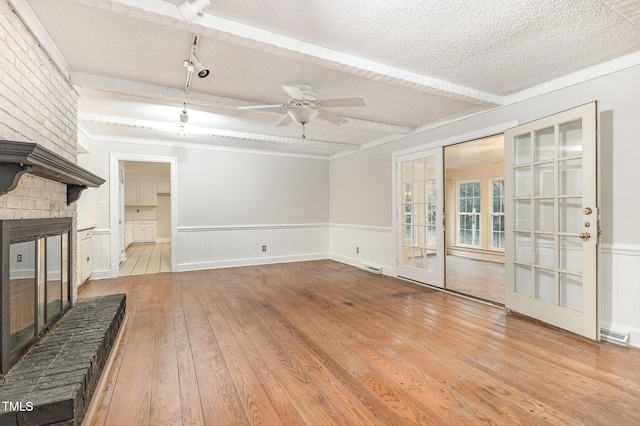 unfurnished living room with beam ceiling, a textured ceiling, light wood-type flooring, ceiling fan, and a fireplace