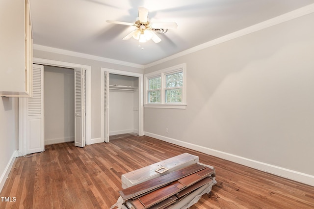 unfurnished bedroom featuring multiple closets, ornamental molding, hardwood / wood-style flooring, and ceiling fan