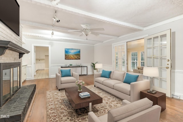 living room with beam ceiling, light hardwood / wood-style floors, a large fireplace, and ceiling fan