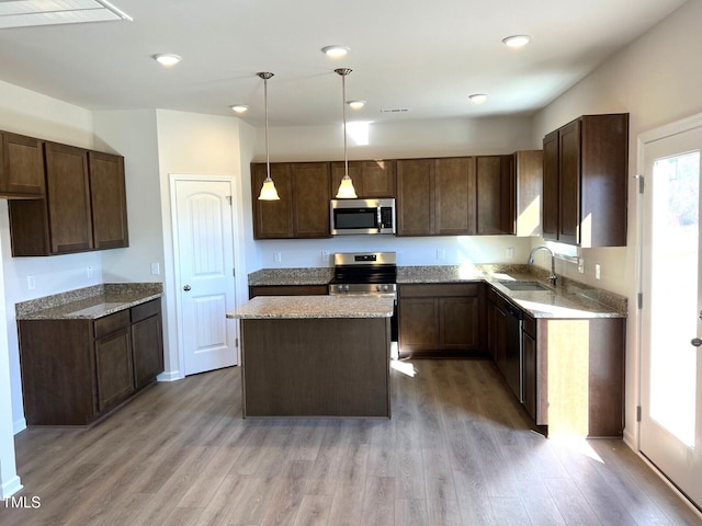 kitchen featuring appliances with stainless steel finishes, decorative light fixtures, sink, a center island, and light hardwood / wood-style flooring