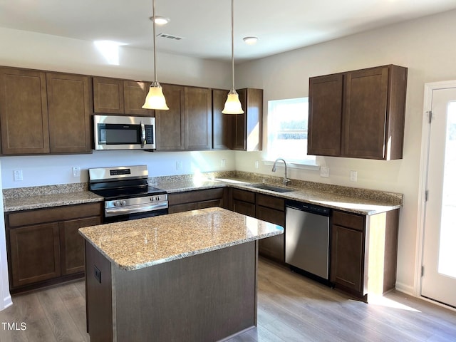 kitchen with dark brown cabinetry, sink, hanging light fixtures, appliances with stainless steel finishes, and light stone countertops