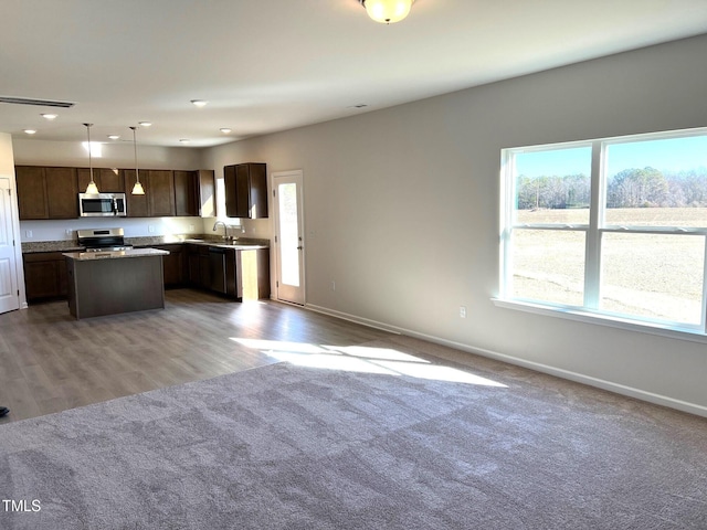 kitchen with sink, hanging light fixtures, stainless steel appliances, a center island, and carpet