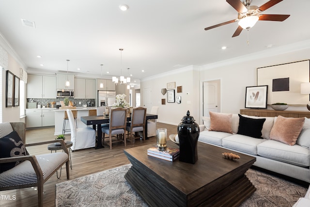 living room featuring ceiling fan with notable chandelier, ornamental molding, and light hardwood / wood-style floors