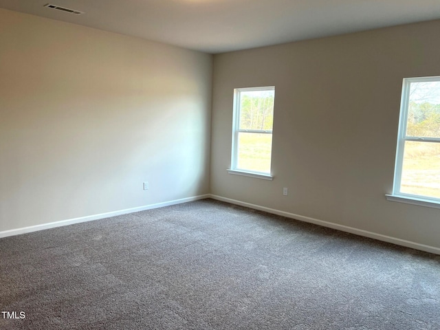 spare room featuring baseboards, visible vents, and dark colored carpet