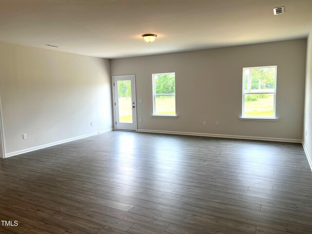 empty room featuring visible vents, dark wood finished floors, and baseboards